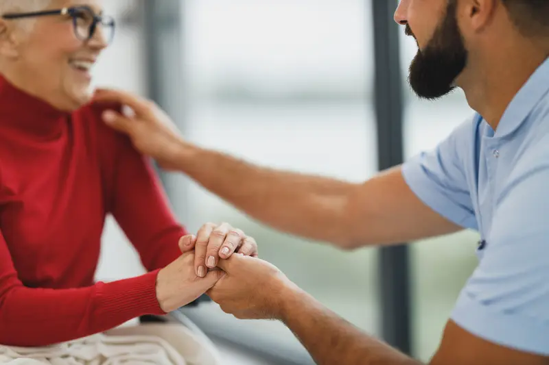 A younger man holding an older woman's hands as they talk